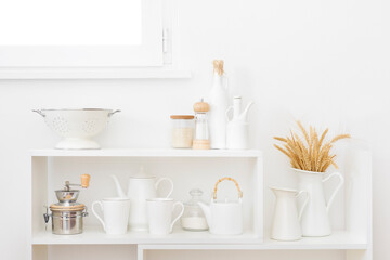 Fototapeta na wymiar White kitchen shelves beneath window with utensils and wheat ears