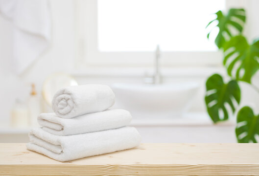 White folded towels on wooden table top in blurred bathroom