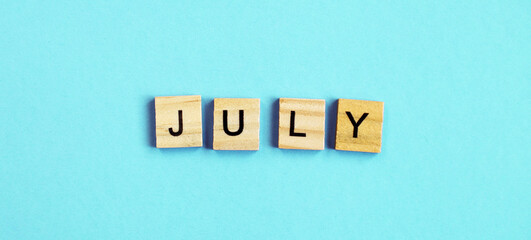 July word made by wooden cubes on a blue turquoise background