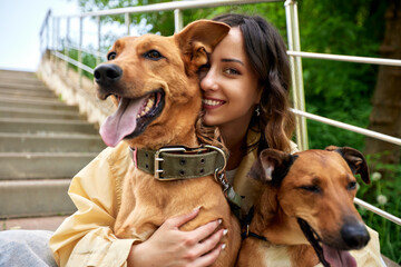 Young charming smiling girl is resting while walking in the park with two golden dogs. The girl...