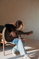 Music and hobbies. A talented young musician girl sits alone and composes songs on the guitar. The girl plays a calm melody on a musical instrument.