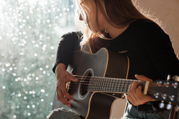 Music and hobbies. A talented young musician girl sits alone and composes songs on the guitar. The...