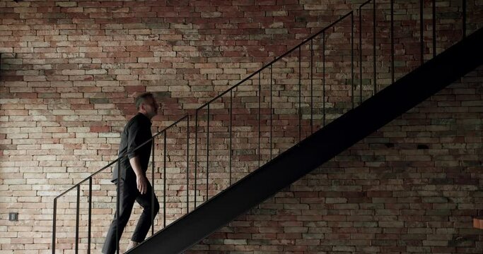 The man was climbing the stairs in the house to the second floor of the house. Old brick wall of brown color in a modern apartment with black stair, damaged masonry as abstract background composition.