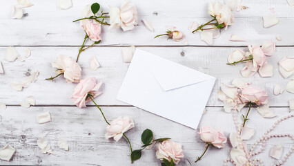 Gift, letter in an envelope and roses on a white wooden white background. Top view, flat lay