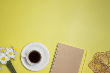 Yellow concept with a cup of coffee, notebook and flowers and copy space.