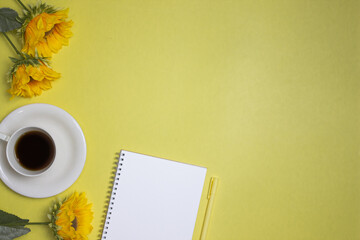 Yellow concept with flowers, notebook, pen and coffee over that yellow background. 