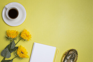 A blank notebook with coffee, yellow pen, flowers over the yellow background. 