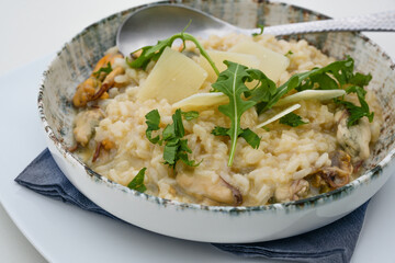 Fototapeta na wymiar Risotto with mussels, arugula and parmesan cheese, Mediterranean meal in a rustic ceramic plate, selected focus, narrow depth of field