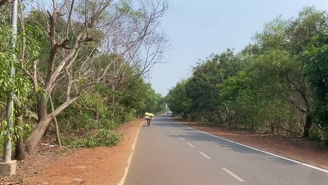 An Indian man cycling alone in an empty highway through the jungle.