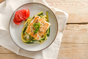 Wild salmon fillet with parsley garnish, zucchini vegetables and tomato on a light plate and a rustic wooden table, healthy low carb diet meal, high angle view from above, copy space