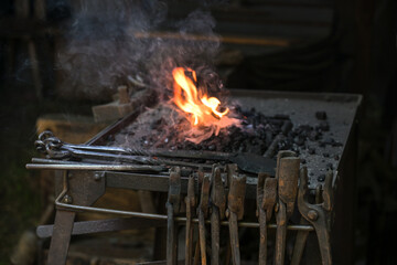 Portable forge of a blacksmith with various rusty tongs and a flaming coal fire at a historic craft...