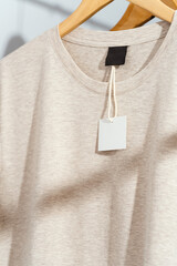 Close up shot of round neckline of beige t-shirt with blank price tag on wooden hanger