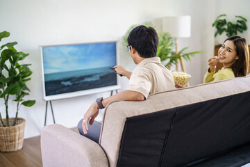 Asian family Watching smart TV together and using remote controller Hand holding popcorn at home with the remote control movie or TV series spending time at home