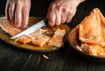 Cooking a delicious fish dish. Cutting red fish on a kitchen cutting board before salting. Hands of a chef with a knife while cleaning a trout