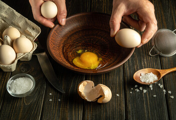 The cook on the kitchen table prepares eggs for a fire or an omelette. Close-up of a chef hand holding an egg