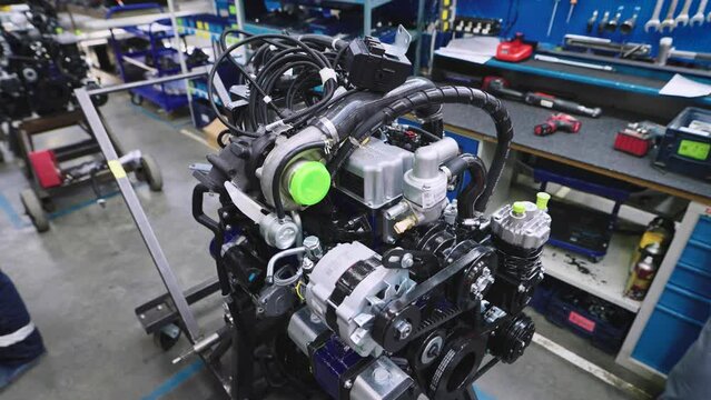 An internal combustion engine in a workshop for assembling commercial vehicles. The engine is mounted on stands, and workers are adjusting and preparing it for installation in a truck or other vehicle