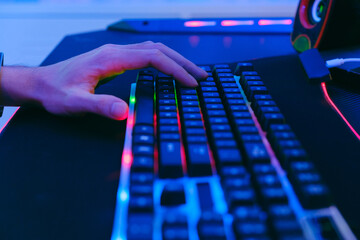 Close-up of professional esports player's hand and push mechanical keyboard with neon light on the large mouse pad on the computer table. Professional gamer equipment.