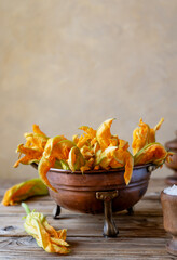Zucchini flowers in a copper antique strainer or colander with wooden utensils. Vertical shot, wooden table, copy space for text