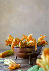 Zucchini flowers in a brass colander with green napkin. Vertical shot, wooden table, copy space for text