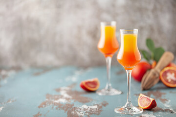Arancello in grappas wineglass, sweet Italian blood orange liqueur, traditional strong alcoholic drink and blood oranges on the light blue wooden background.