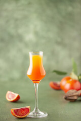 Arancello in grappas wineglass, sweet Italian orange liqueur, traditional strong alcoholic drink and oranges on the green wooden background.