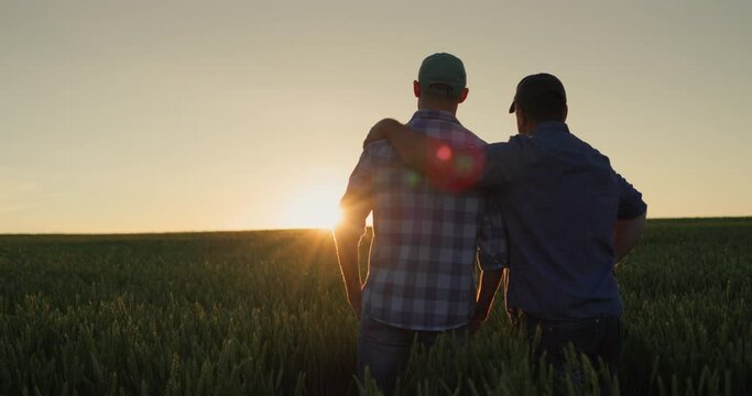 Father farmer hugging his adult son and watching the sunset over the field together