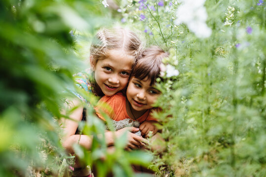 Cute children having fun outdoors. Two girls are playing hide and seek in the summer garden. Children among green nature. Little explorers.