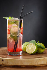 Refreshing cocktail in a glass with lime, strawberries, basil, mint and two black straws on a...