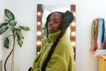 portrait of an African woman  with a stylish braids in a green coat  in the dressing room by the...