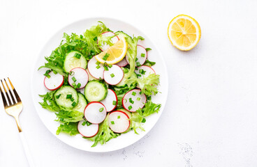 Healthy summer salad with fresh radishes, cucumbers, lettuce and green onion with greek yogurt dressing, white table background, top view