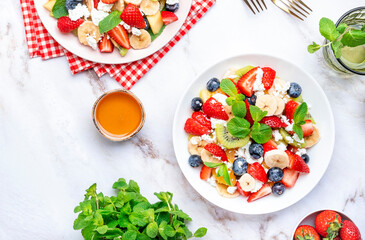 Fresh fruit and berry salad with cottage cheese, strawberries, blueberries, kiwis, oranges and mint leaves with honey dressing, marble table background, top view