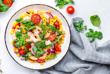 Fresh tasty salad with shrimps, sweet corn, avocado, red cherry tomatoes, lamb lettuce and onion on white table background. Top view