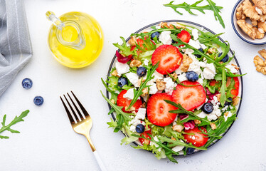 Strawberry salad with arugula, lettuce, blueberries, feta cheese and walnuts, white table. Fresh useful dish for healthy eating