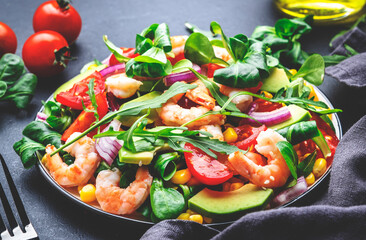 Fresh salad with shrimps, sweet corn, avocado, red tomatoes, lamb lettuce and onion on black table background. Top view