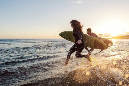 Couple is running into the water with surfboards.