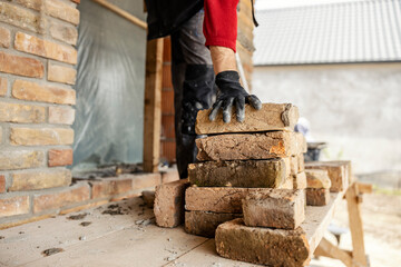Cropped picture of a housebuilder taking brick from a pile on a building area.