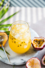 Glass of Iced passion fruit soda with lemon and passion fruit half slice on a light background, refreshing drink or beverage with ice