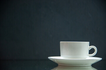 Front view of white set of coffee cup and saucer on the left side on dark wave background with free...