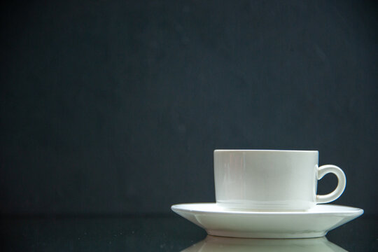 Front view of white set of coffee cup and saucer on the left side on dark wave background with free space