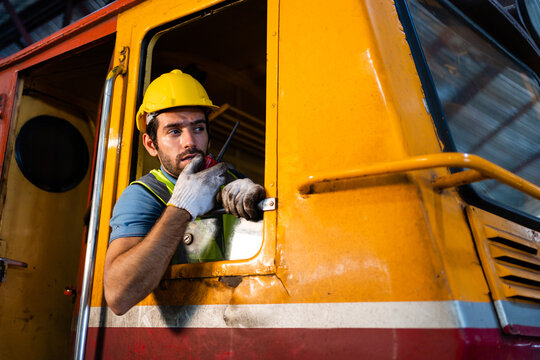 A Handsome Train Driver Uses A Walkie-talkie Or Walkie-talkie In The Interior Room To Control The Train. Professional Railway Engineer.