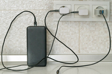 Three cables for charging electrical devices are plugged into electrical outlets, one of them charges the power bank