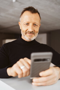 55-Year-Old Man with Turtleneck Looks Positively at His Smartphone