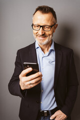 Older Businessman with Glasses Standing in Front of a Brown Wall, Looking at Smartphone with Copy Space