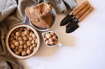 Edible caramel clay stones on a wooden round plate and brown clay stones with small garden shovels on a white background flat lay