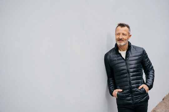 Older Man Leaning Relaxed Against A Concrete Wall, Looking To The Side