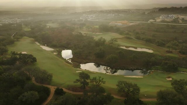 Aerial drone pull away over Texas Hill Country golf course green fairway with suburban community in background