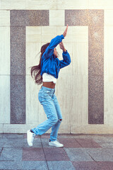 Photo shoot of stylish caucasian hip hop dancer posing having fun in blue jacket, jeans, black top and white tshirt, enjoy the urban town as background. City buildings shooting of moving fitness model