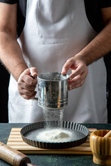 Half body shot of male chef wearing his uniform sifting flour in the kitchen in close up view