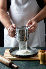 Half body shot of male chef wearing his uniform sifting flour in the kitchen in front view
