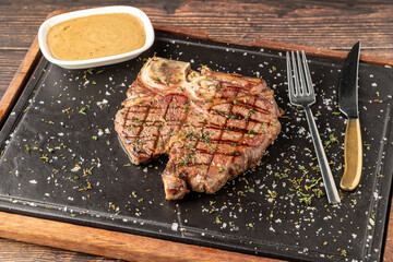 Top view of T-Bone Steak served on stone plate with sauce on the side